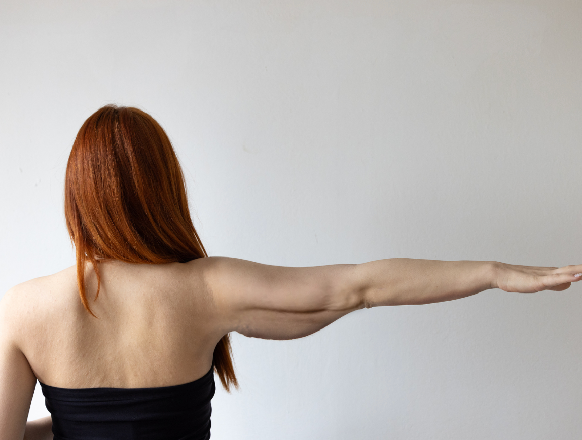 Person seen from behind with one arm extended straight out against a plain white wall