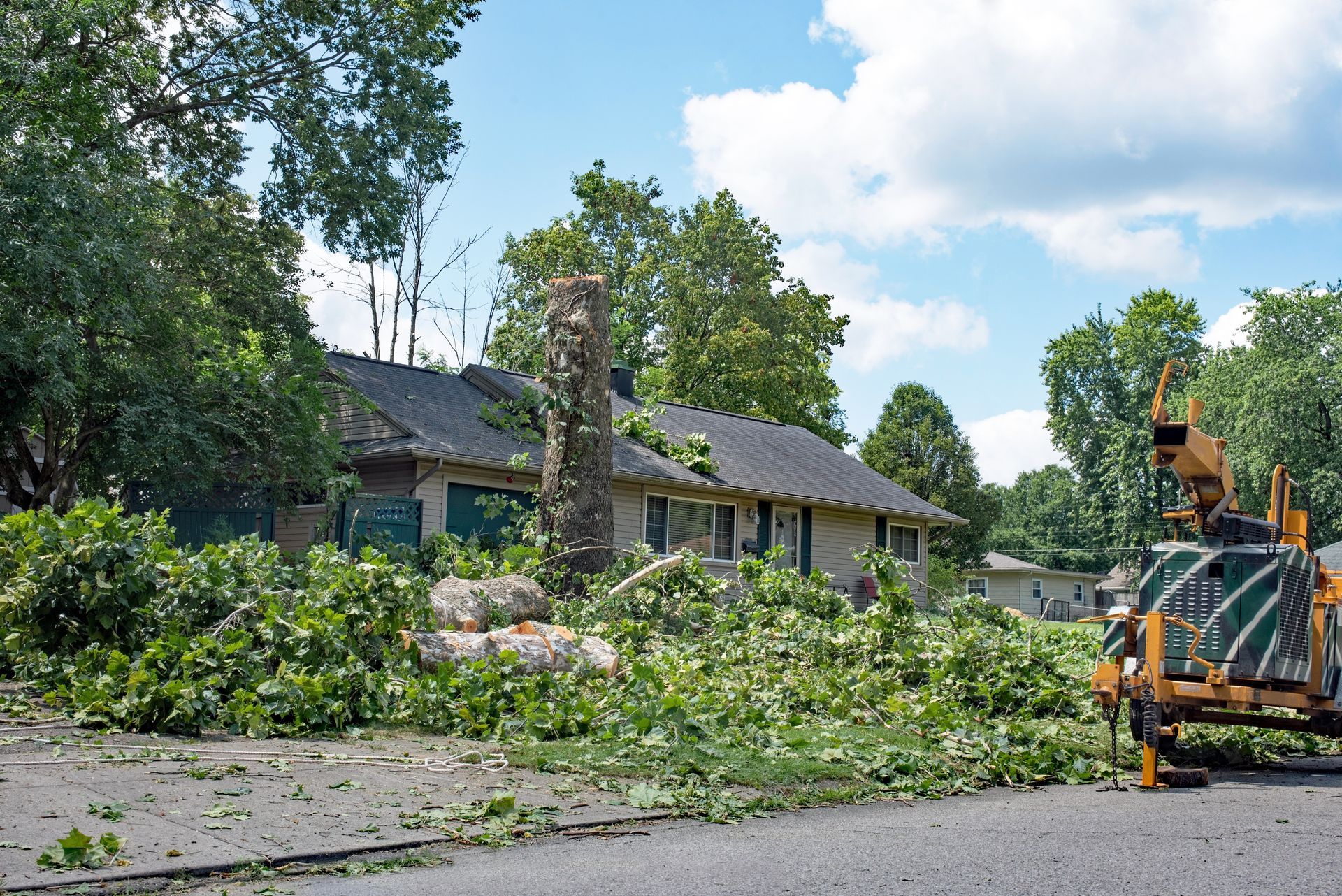 Storm-damaged street with fallen tree branches and a utility truck clearing debris near houses.