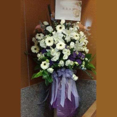 以白色百合、雛菊和紫色點綴的花束；頂部放著一張卡片。