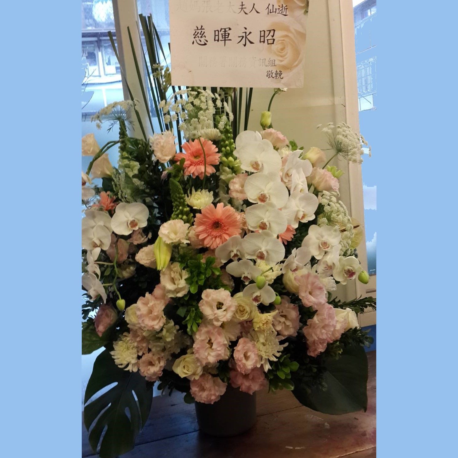 以白色、粉紅色和橙色花朵為主的花束，包括蘭花和非洲菊，並附有中文標誌。
