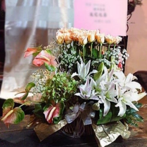 籃子裡的花束，包含桃色玫瑰、白色百合、粉紅紅掌和綠色繡球花。