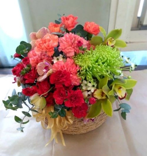 編織籃中的插花。康乃馨、蘭花和菊花，顏色有紅色、橙色、綠色和黃色。