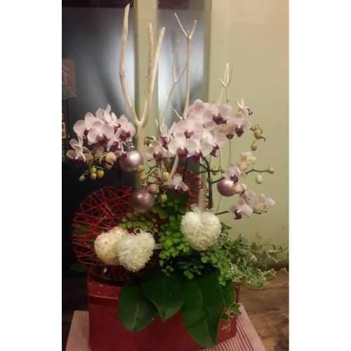 紅色盒子裡擺放著一束鮮花，花材包括蘭花、白色樹枝、紅色點綴和心形裝飾。
