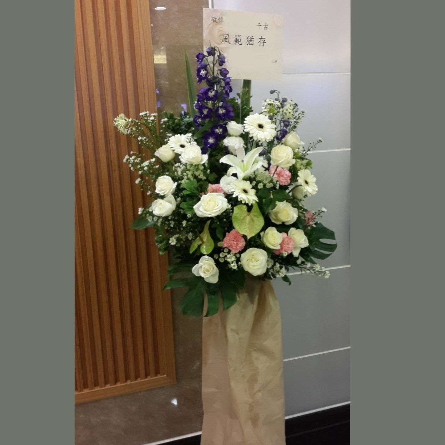 花束，由白色和粉紅色玫瑰、百合和藍色飛燕草組成。米色布料包裝。