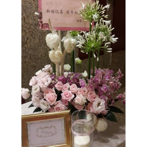 桌上擺放著一束花卉擺設，旁邊立著一塊牌子，牌子裝在一個金色的相框裡。