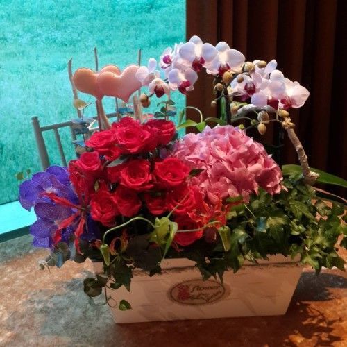 白色長方形花盆中的插花：紅玫瑰、粉紅色繡球花、白色蘭花、常春藤。