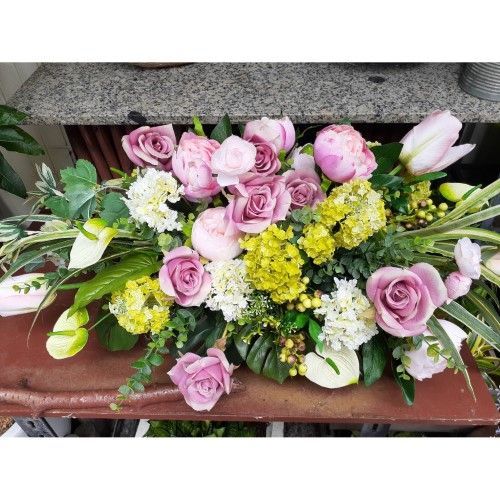 桌上擺放著粉紅色玫瑰、牡丹以及黃色和白色花朵組成的花束。