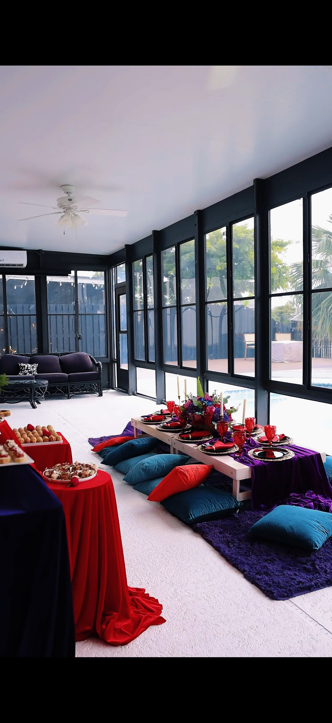 Room with tables draped in red and purple, floor seating, and large windows.