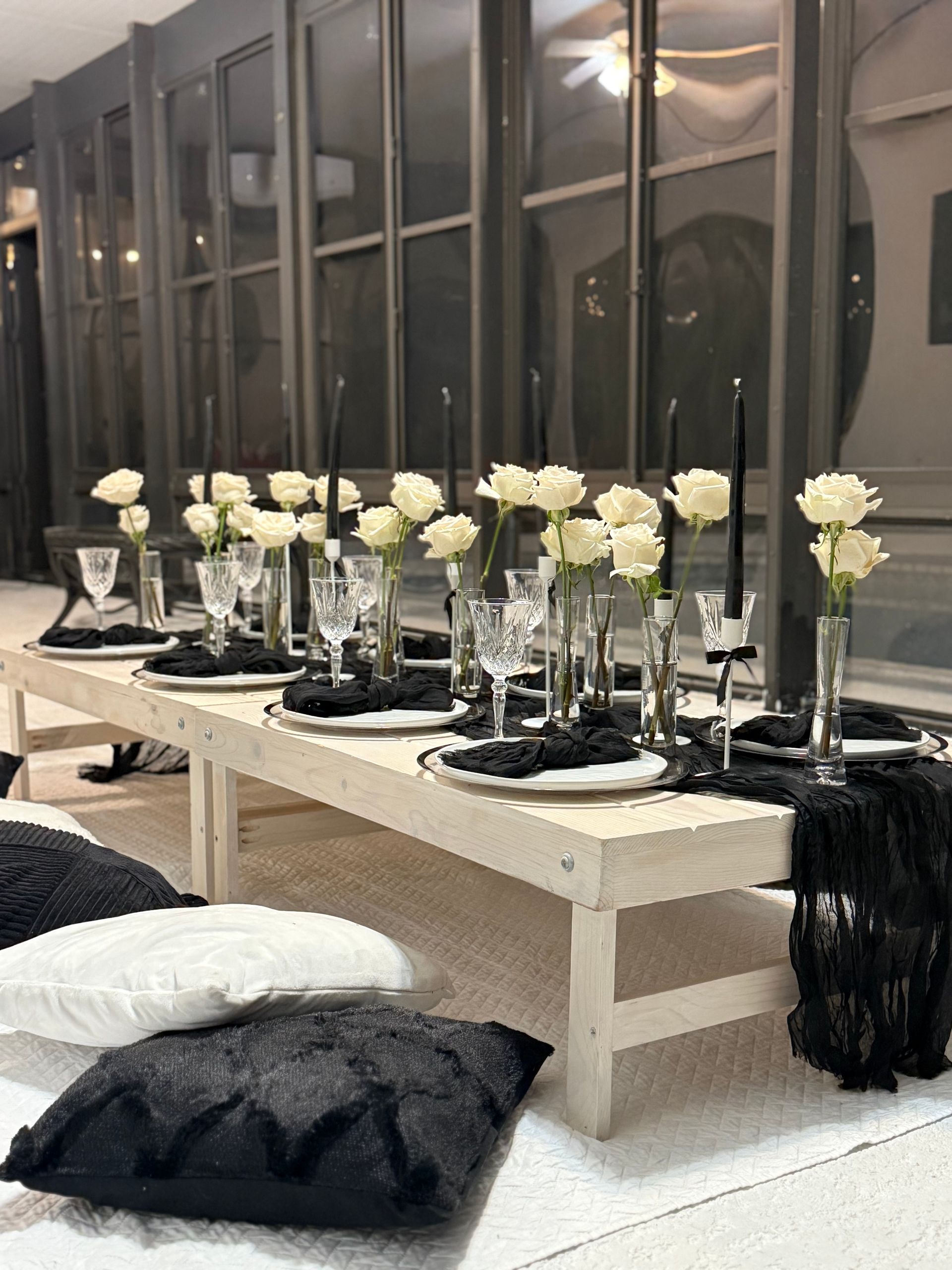 Low table set for dinner with white roses, black candles, and pillows.