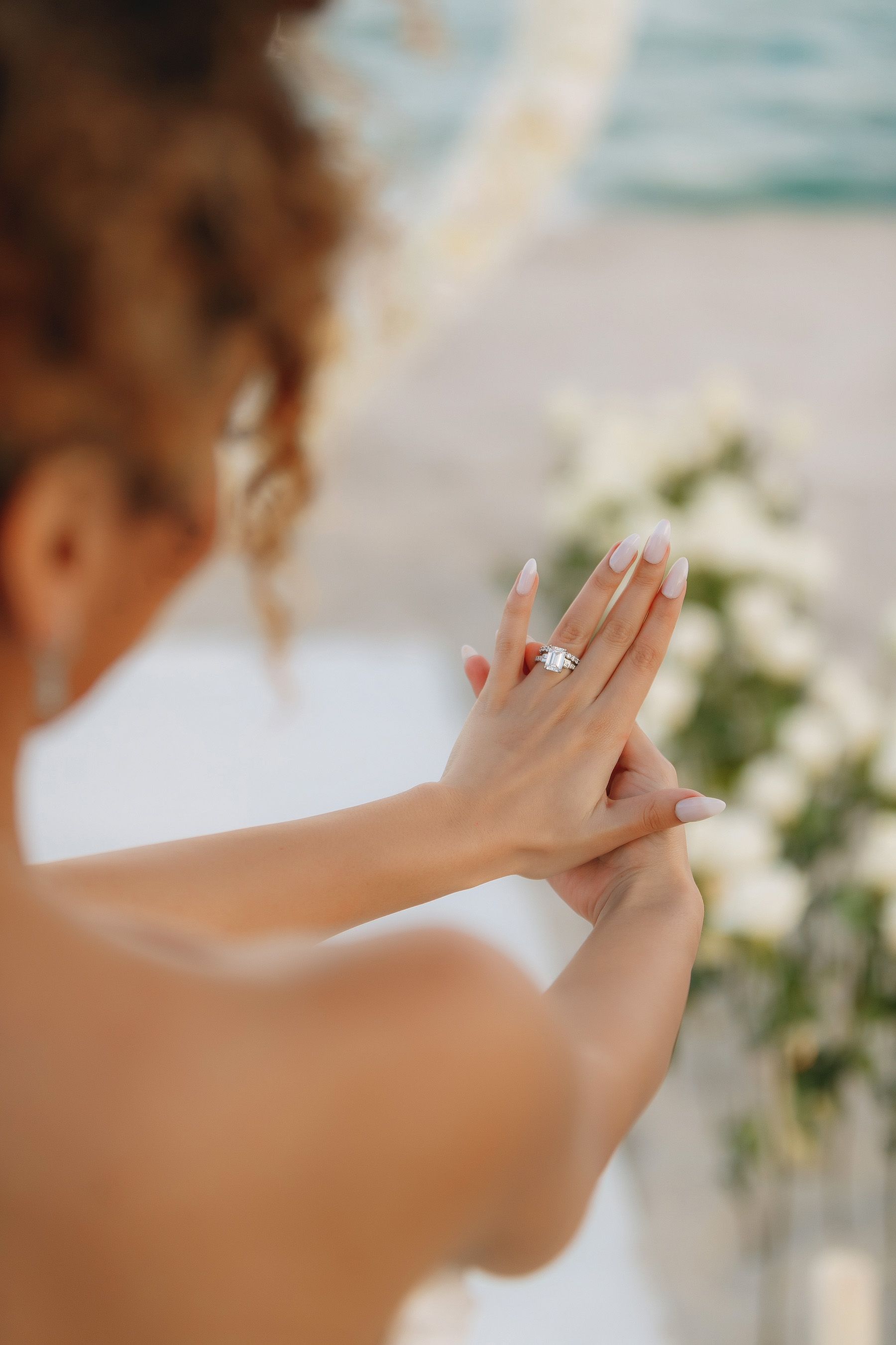 Woman showing off engagement ring with floral backdrop. Beach setting, sunny.