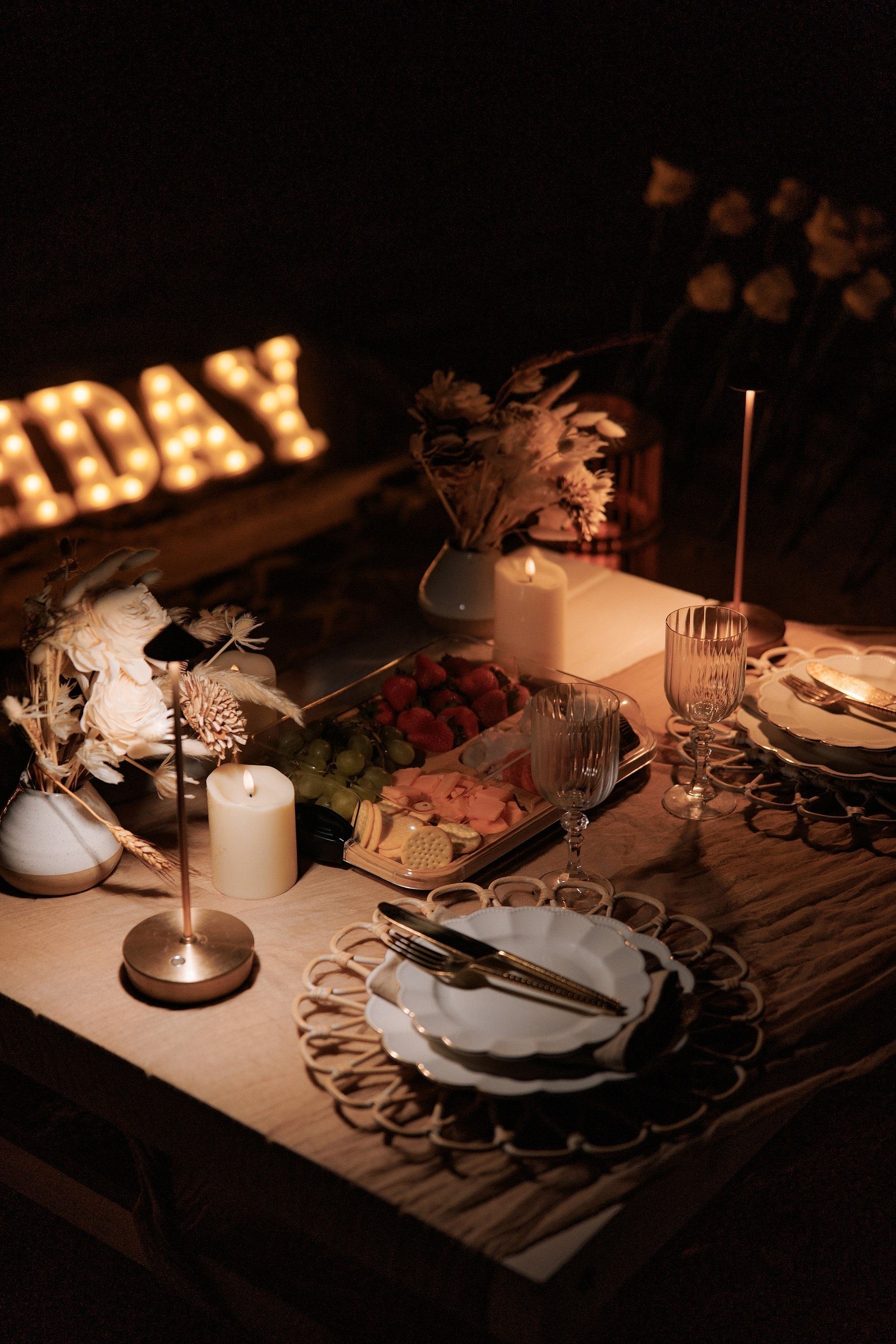 Romantic candlelit dinner table set for celebration. Fruit platter, elegant plates,
