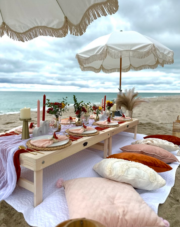 Beach picnic setup with a low table, cushions, and parasols.