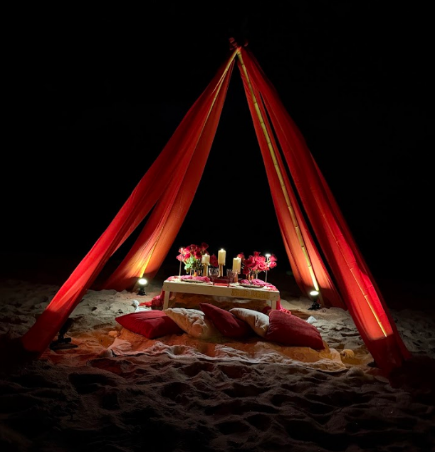 Romantic candlelit picnic on the beach at night, under draped red fabric.