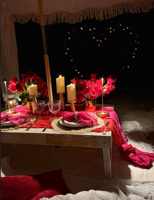 Romantic candlelit dinner setup with red roses, heart-shaped lights, and a table.
