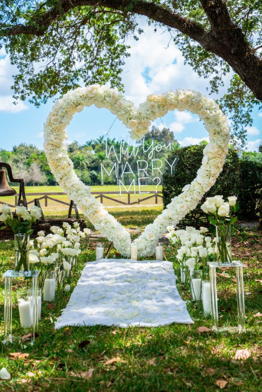 Wedding ceremony setup with a heart-shaped floral arch and aisle of candles and flowers.