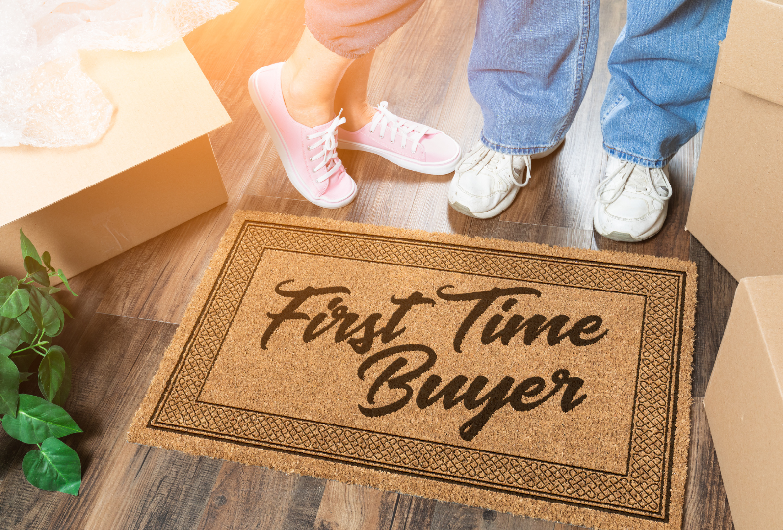 A couple are stood by a doormat that says First Time Buyer