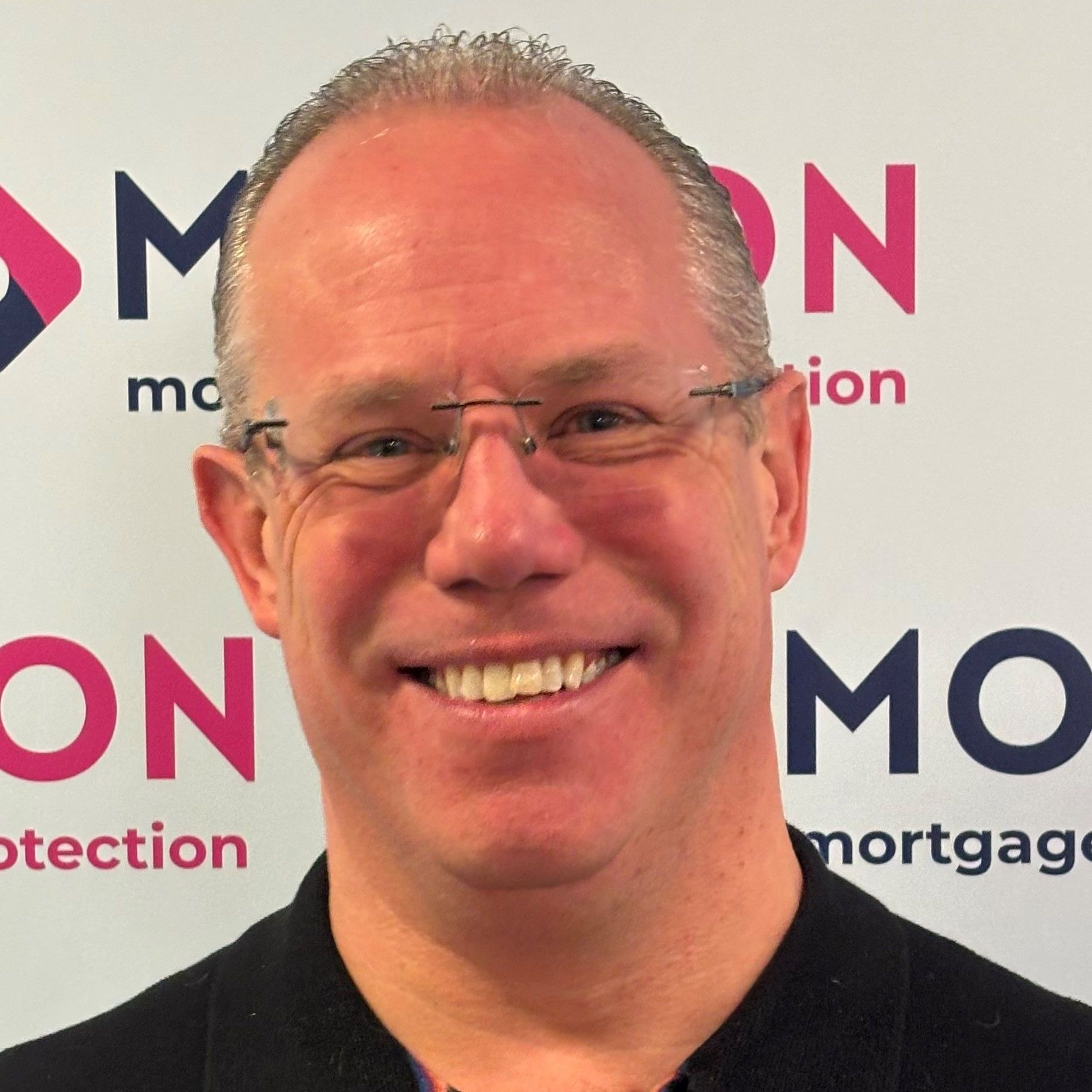 Dave Howarth of Motion Mortgages & Protection is smiling in front of a branded backdrop