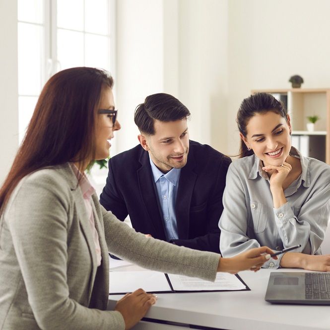 A man and two women are sitting at a table with a laptop.