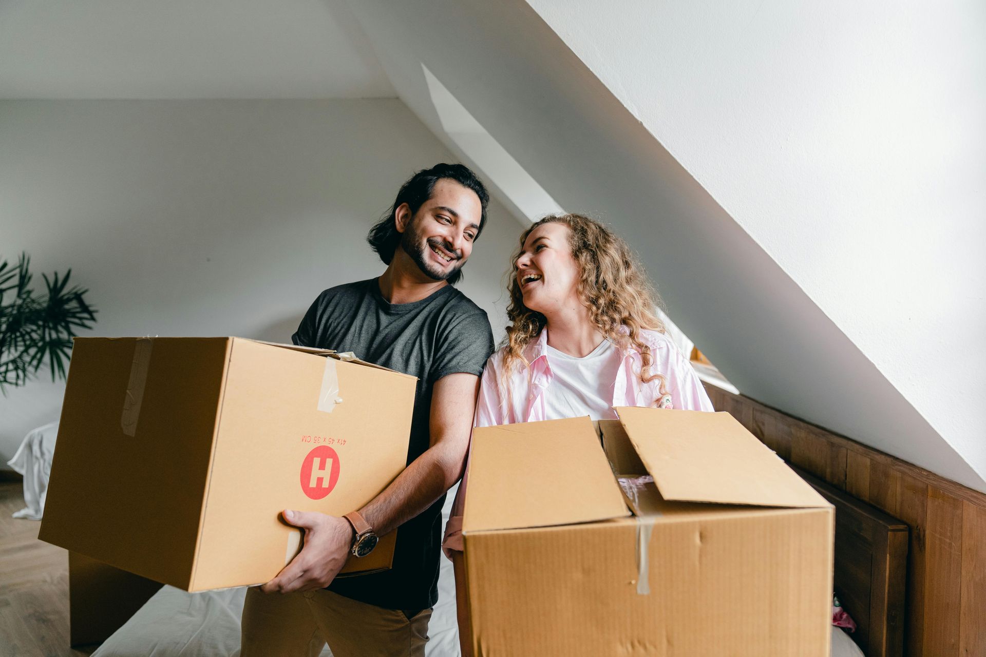 A young couple are smiling and laughing as they bring moving boxes into their first home