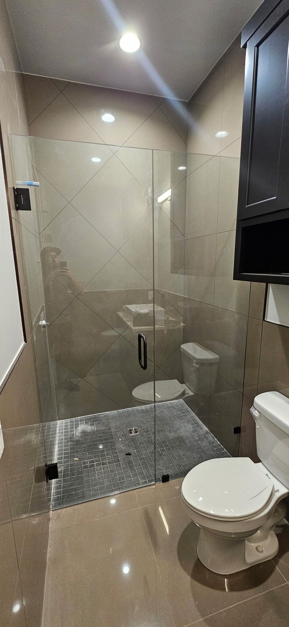 Modern bathroom with glass shower, beige tile, and wall-mounted toilet beside a dark cabinet.