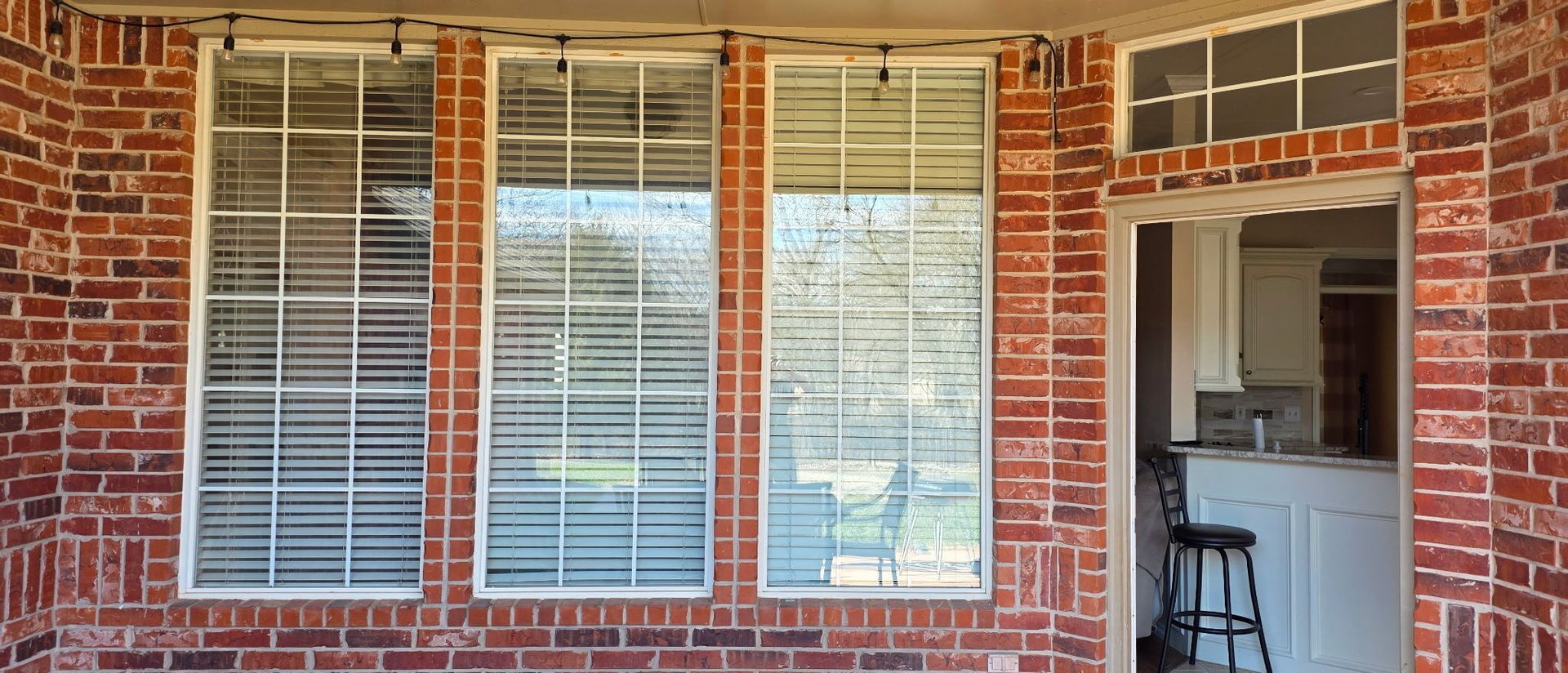 Brick house exterior with white-trimmed windows, shutters, and an open doorway to a screened porch