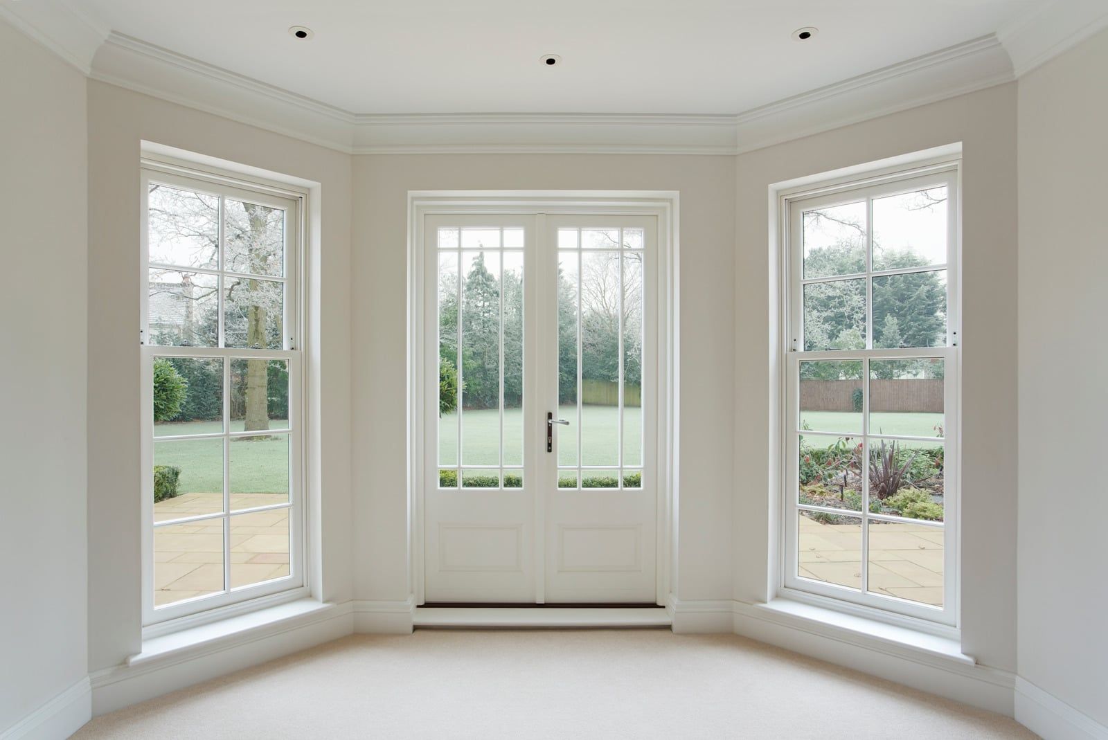 Bright bay window alcove with French doors and three tall windows overlooking a green yard.