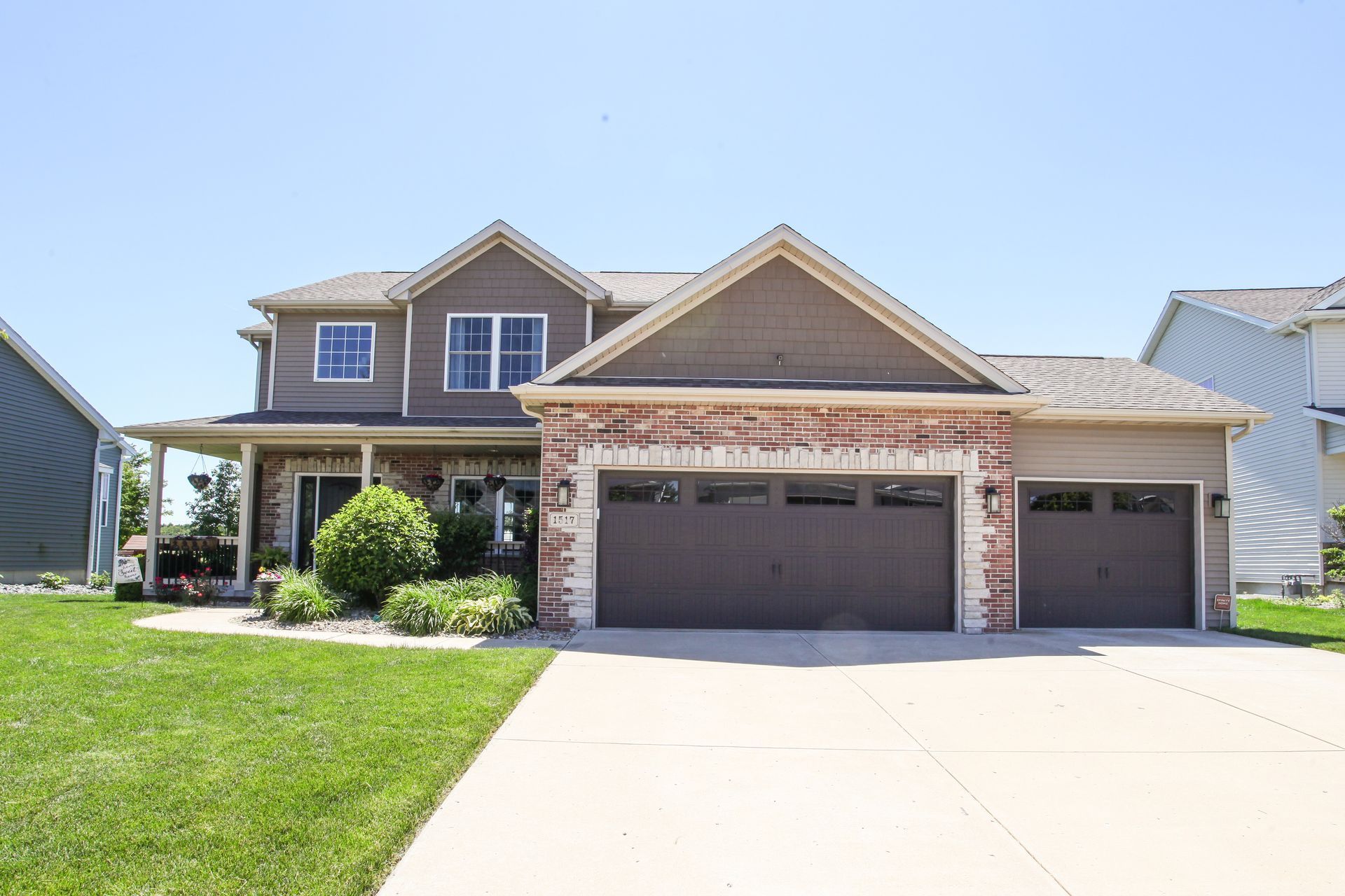 Suburban two-story brick house with a three-car garage and a green lawn under a clear blue sky