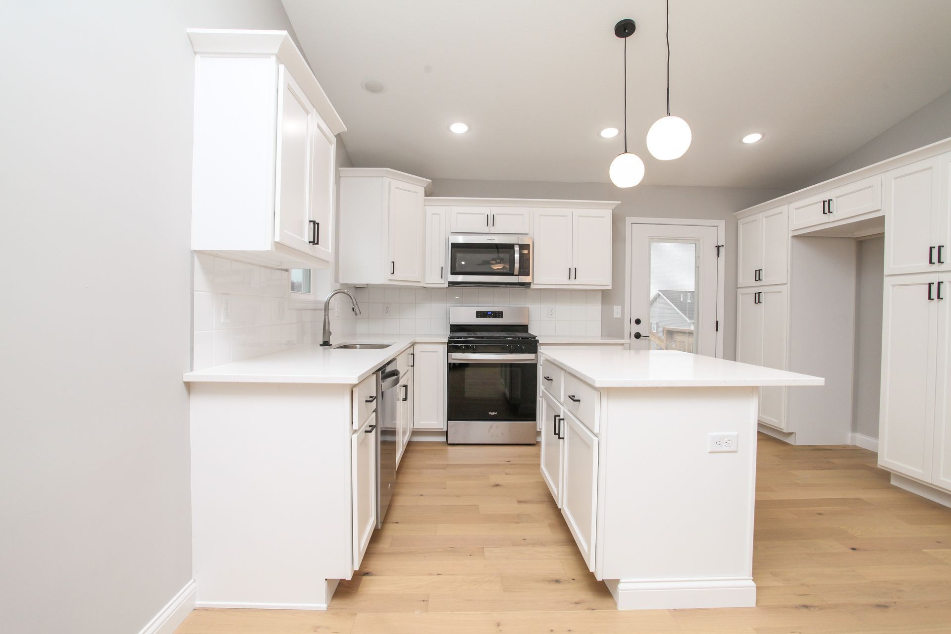 Bright modern white kitchen with island, stainless steel appliances, and light wood floors