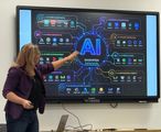 Woman points at a large screen showing an AI diagram and icons in a classroom.
