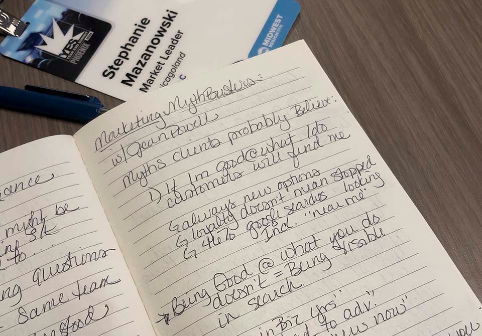 Open notebook with handwritten notes beside a blue smartphone and a book on a desk