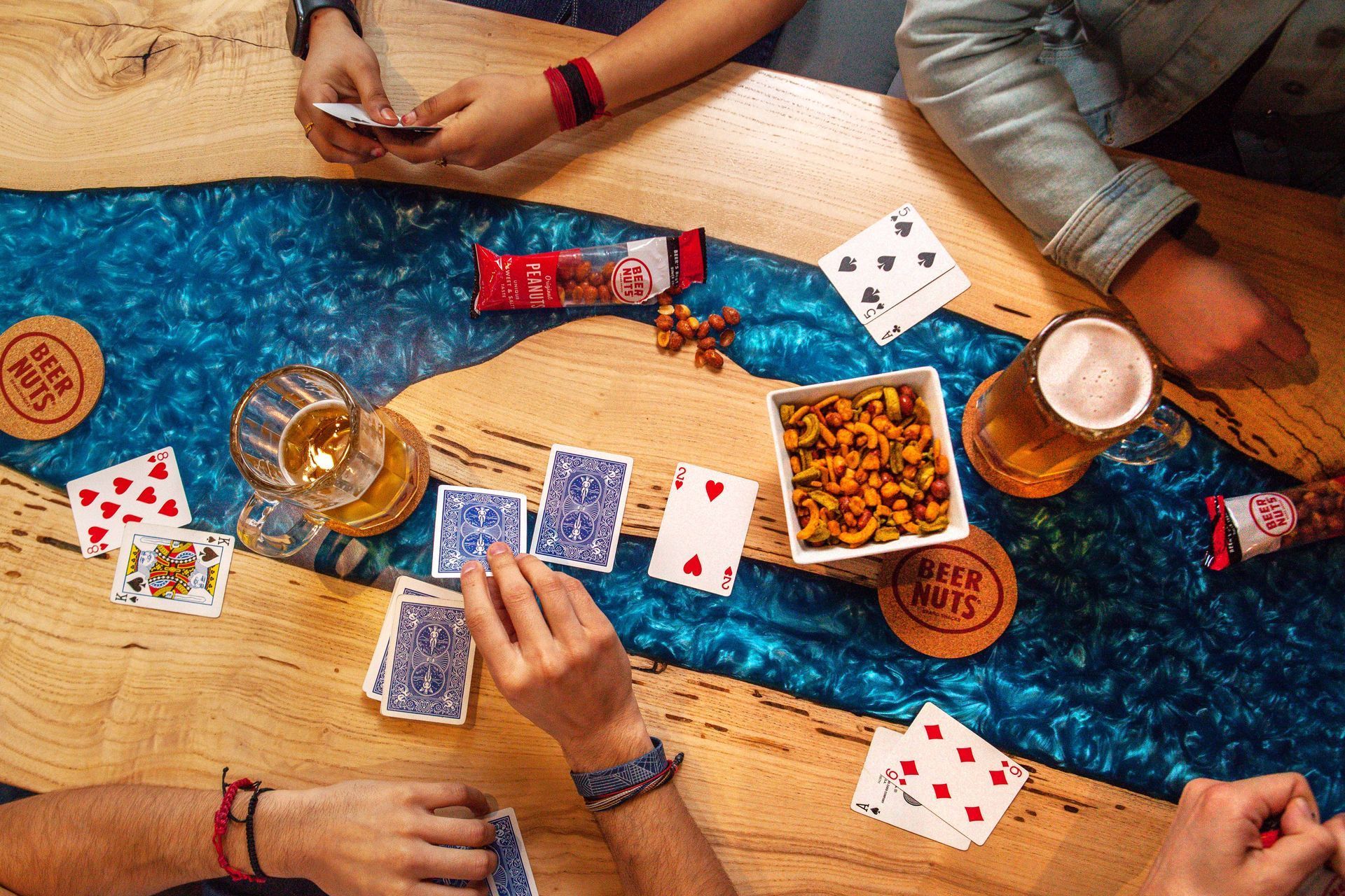 Friends playing cards around a wooden table with snacks and drinks on a blue rug