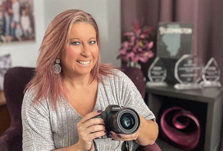 Smiling woman with a camera sitting in a chair with awards in the background