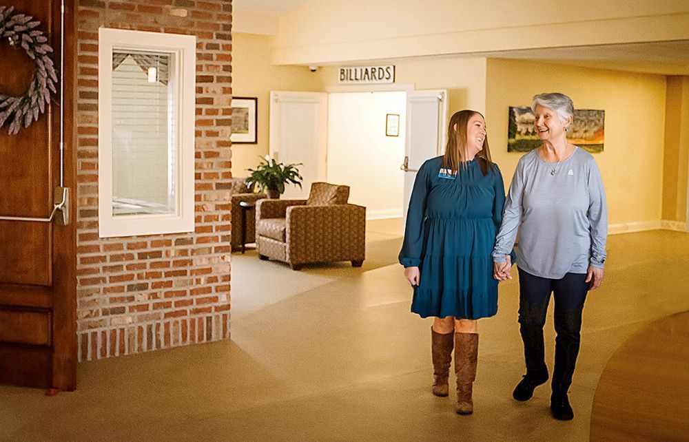 Two people walking in a bright lobby, chatting near brick walls and armchairs.