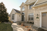 Suburban house exterior with beige brick, front entry, windows, and a small landscaped walkway