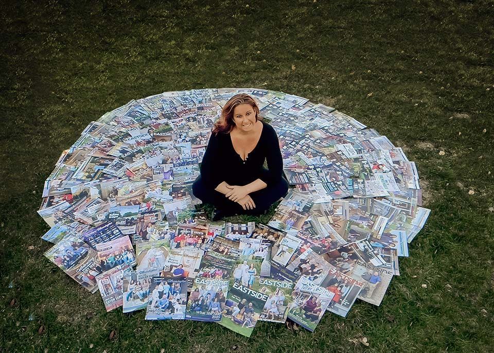 Person sitting cross-legged on grass inside a circle of scattered magazines, viewed from above.