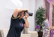 Photographer aiming a DSLR indoors beside a chair and potted plant