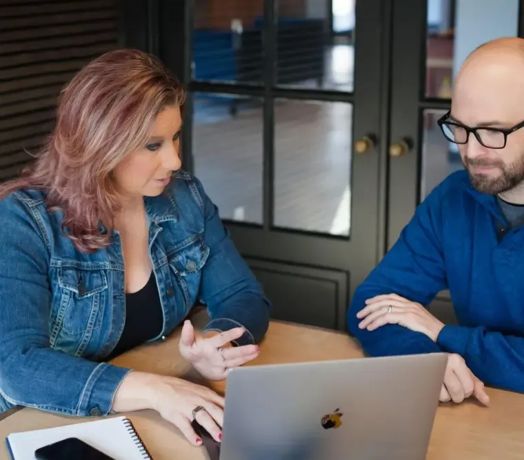 Two colleagues discussing over a laptop at a table in an office setting