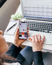 Person holding a smartphone beside a laptop, viewing social media at a desk.
