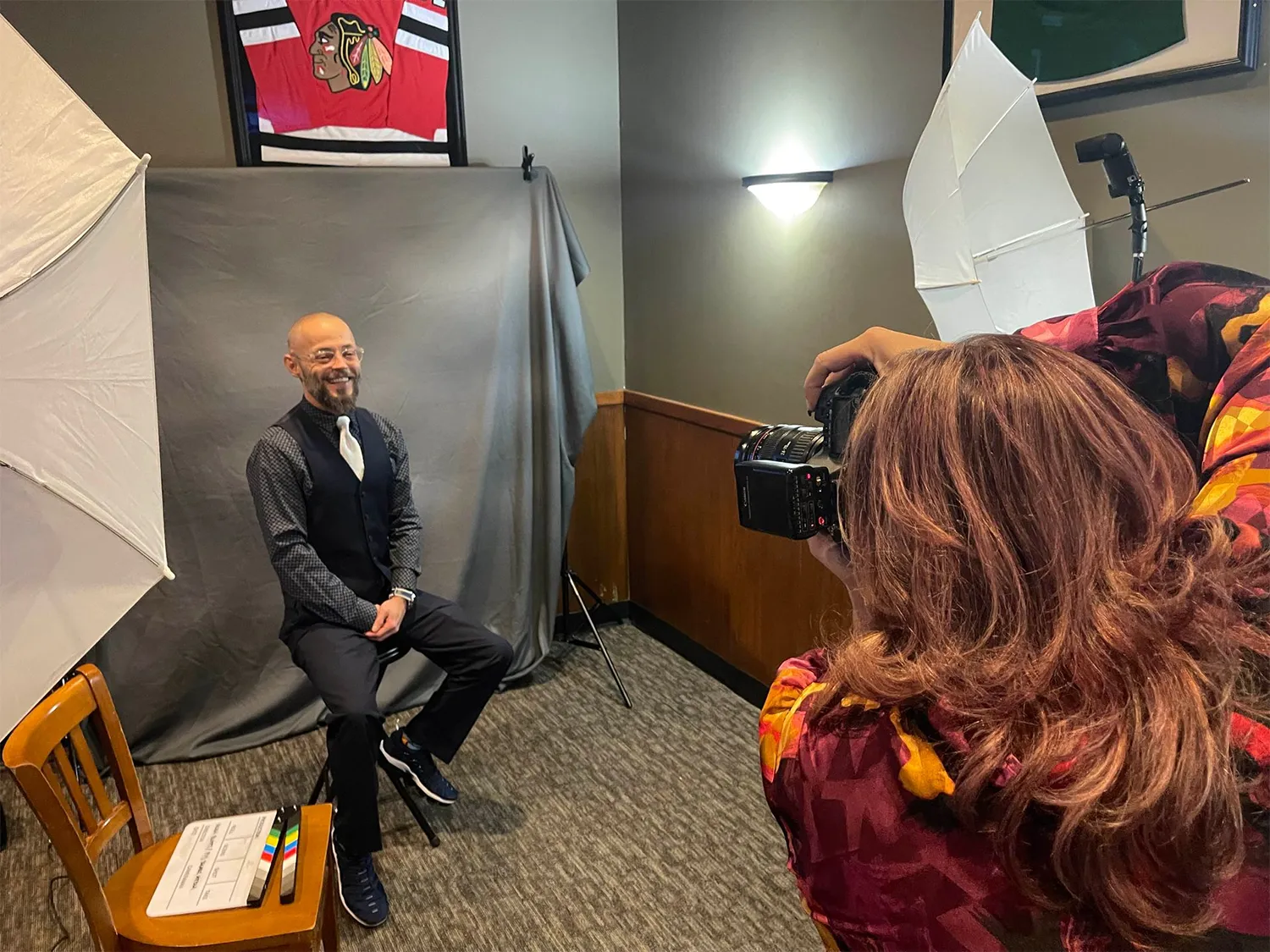 Photographer taking a portrait of a seated man in a studio with backdrop lights and softboxes.