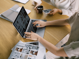 People collaborating around a laptop and printed photos at a table, with a phone and coffee cup nearby