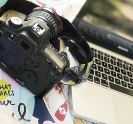 DSLR camera resting on a laptop keyboard beside a colorful notebook and mug