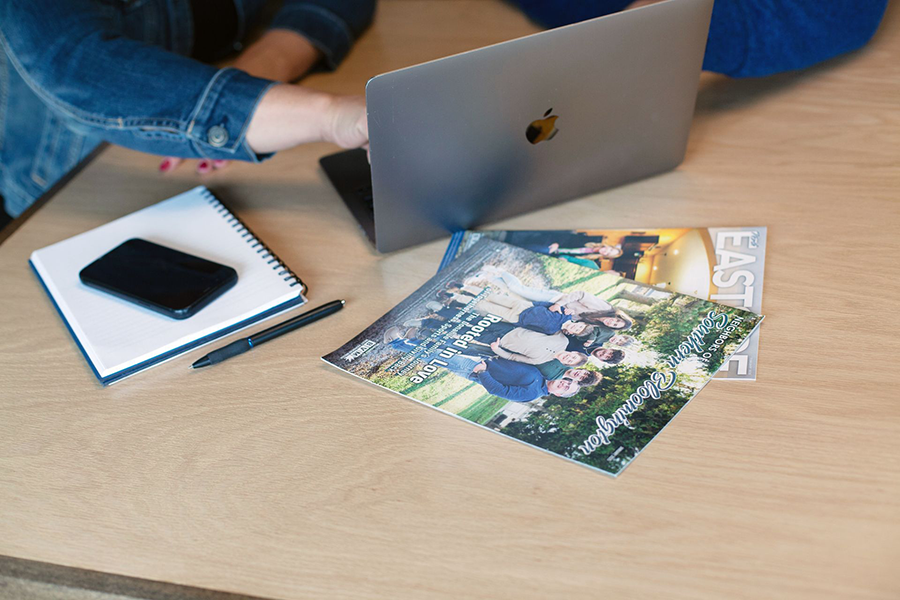 Laptop, notebook, phone, and pen on a desk beside a magazine.