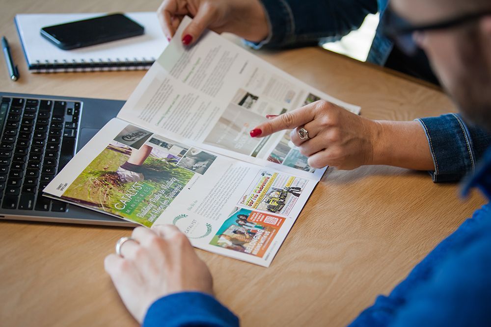 People reviewing a magazine spread at a desk with a laptop and notebook