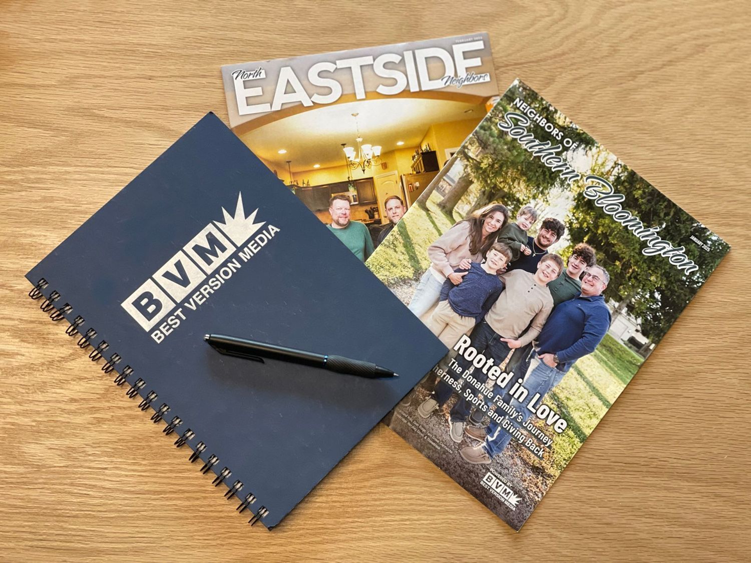 Brochures and a pen on a wooden table, including Eastside and People & Life covers