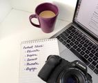Desk with purple mug, notebook listing content ideas, Canon camera, and laptop keyboard