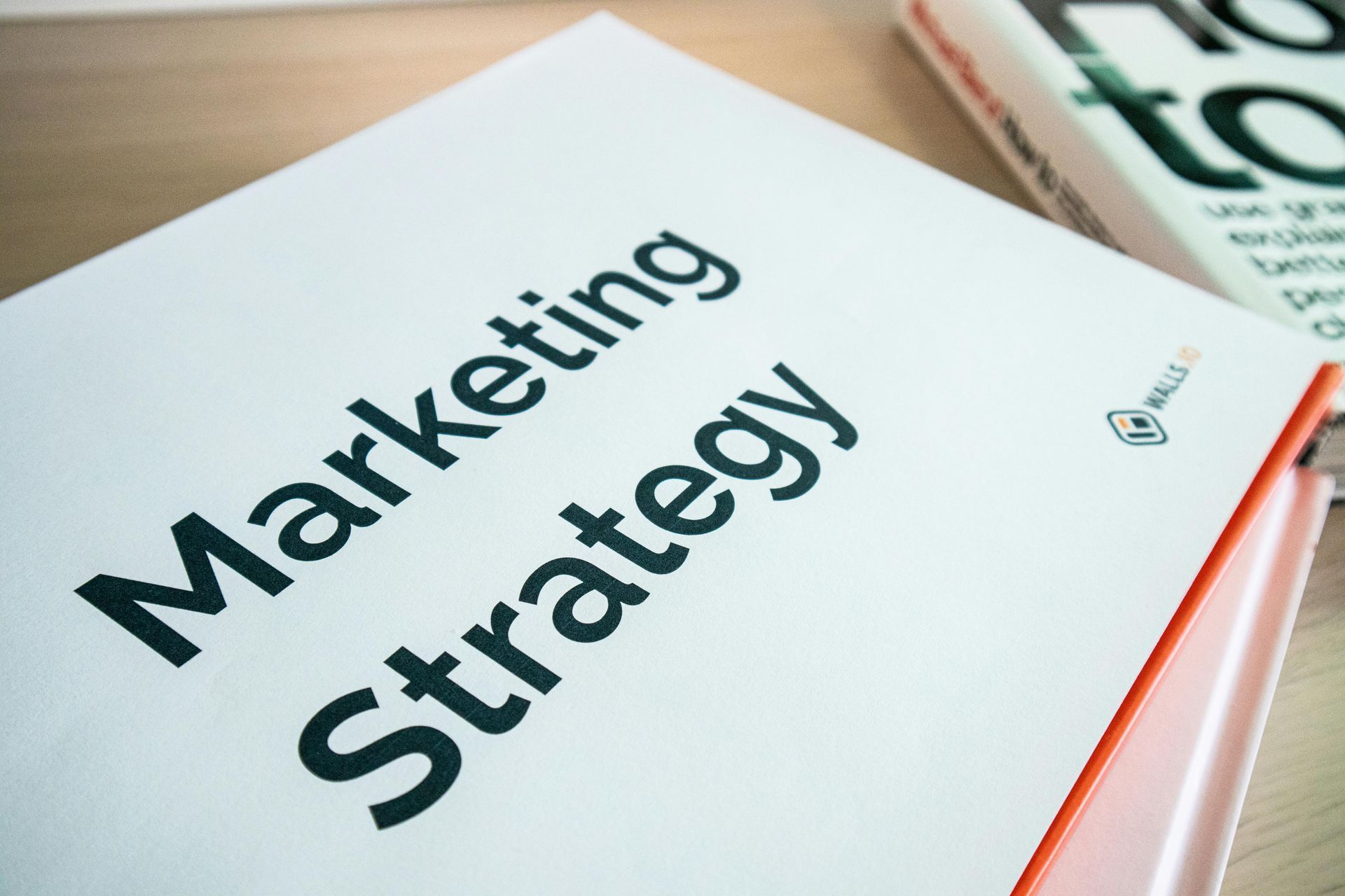 Marketing Strategy booklet on a desk, white cover with black text and orange edge