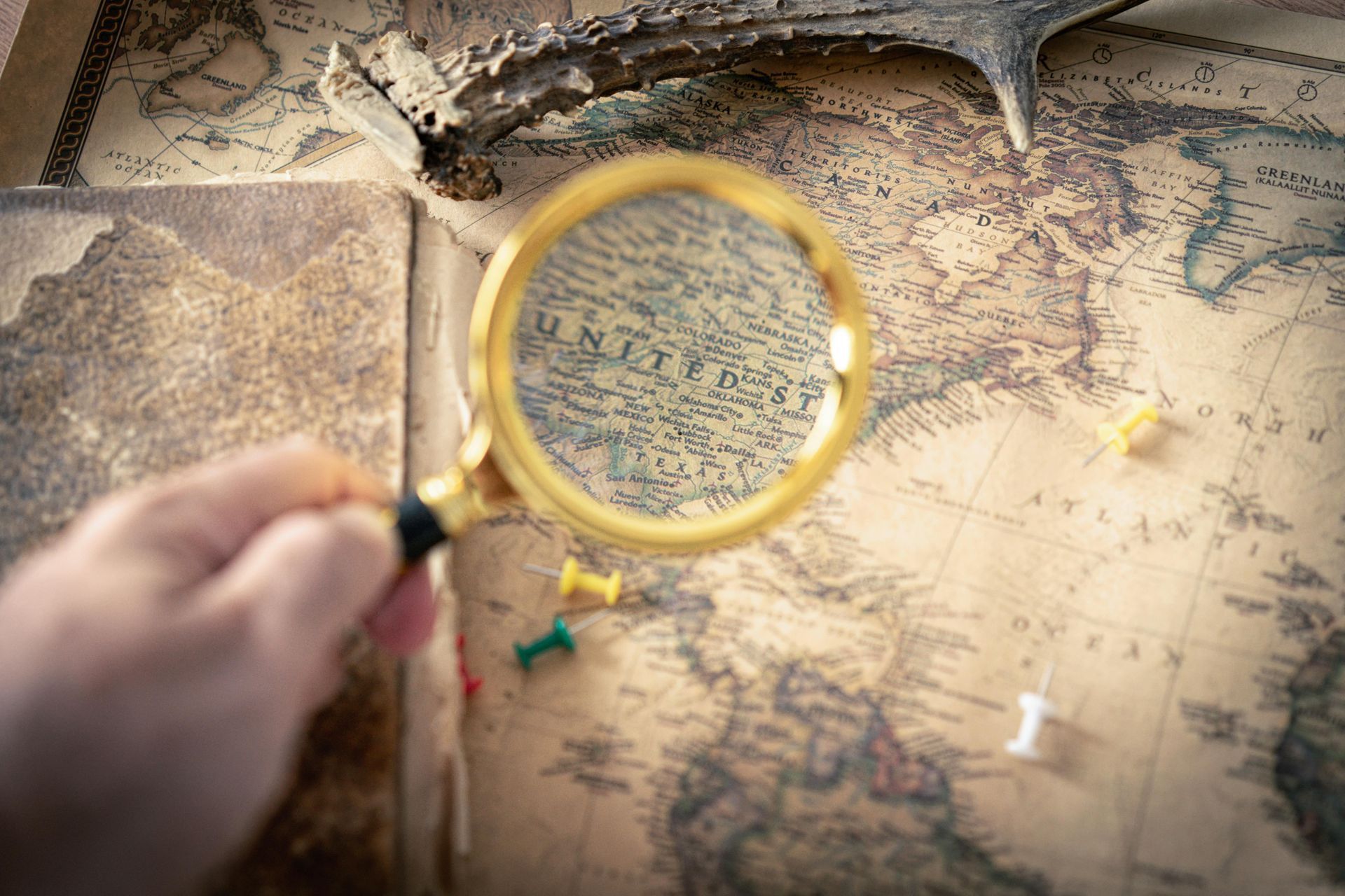 Hand holding a magnifying glass over an old map, with a small lizard nearby.