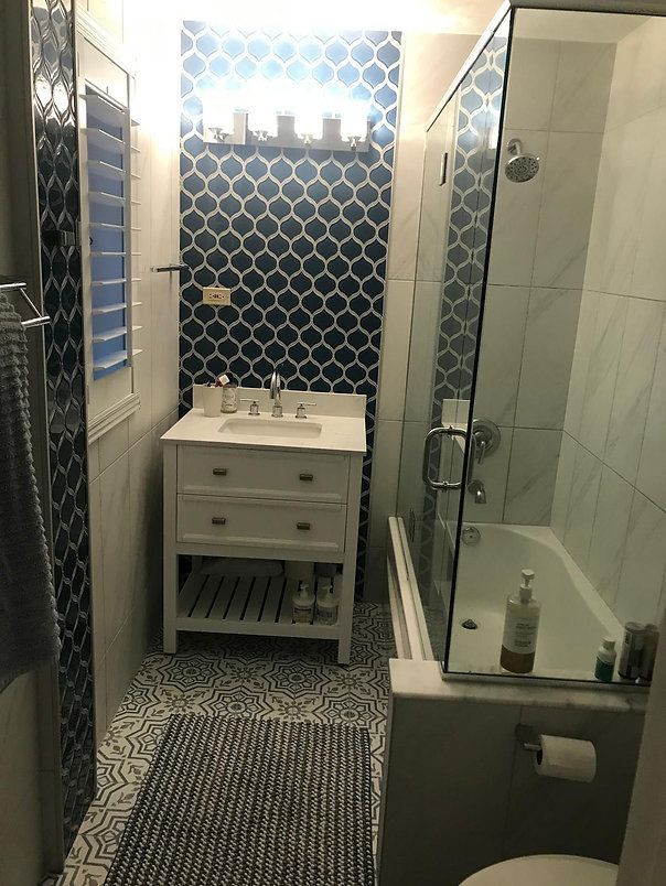 Bathroom with patterned navy tile accent wall, white vanity, glass shower, and blue rug.