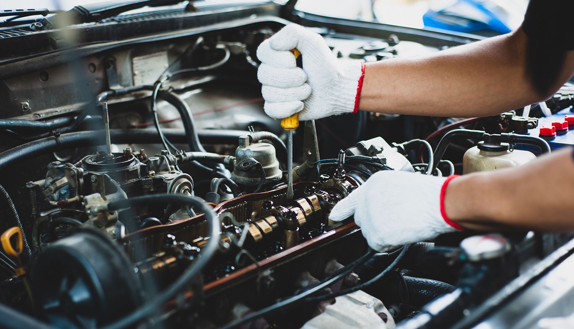 Hands in white gloves using a screwdriver on a car engine.