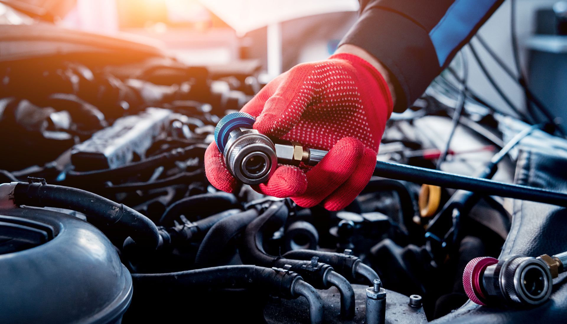 Mechanic in red gloves working on a car engine, connecting hoses.